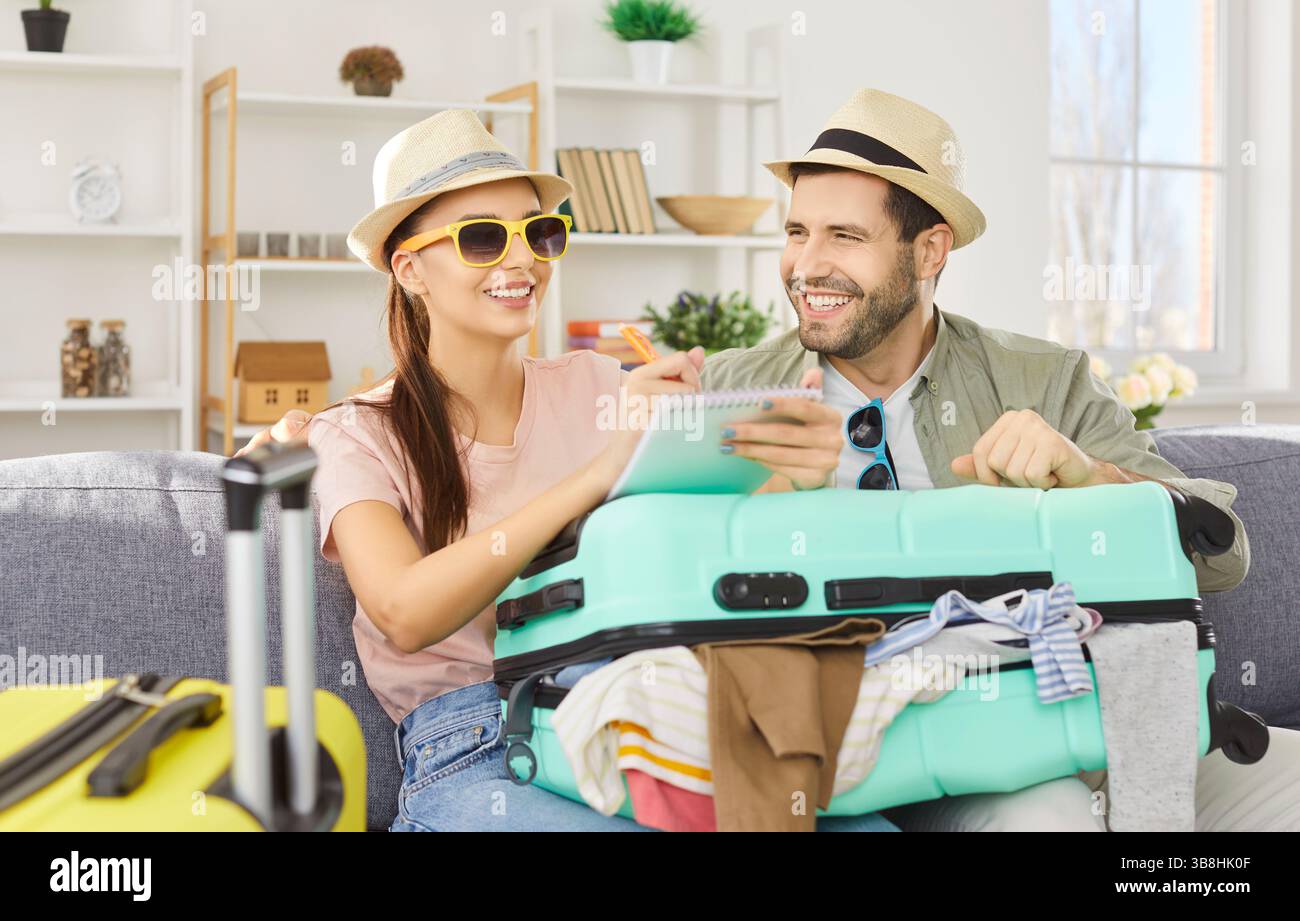 Ein Paar sitzt zu Hause auf dem Sofa und hat den Koffer gepackt, um eine Einkaufsliste für den Urlaub zu machen Stockfoto