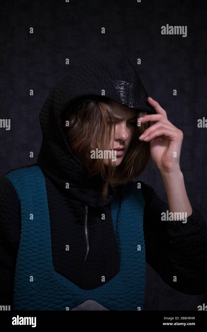 Porträt eines Models mit Hoodie. Haare im Gesicht, berühren eine Kapuze und dunkle Stimmung während eines coolen, modischen Fotoshootings. Stockfoto