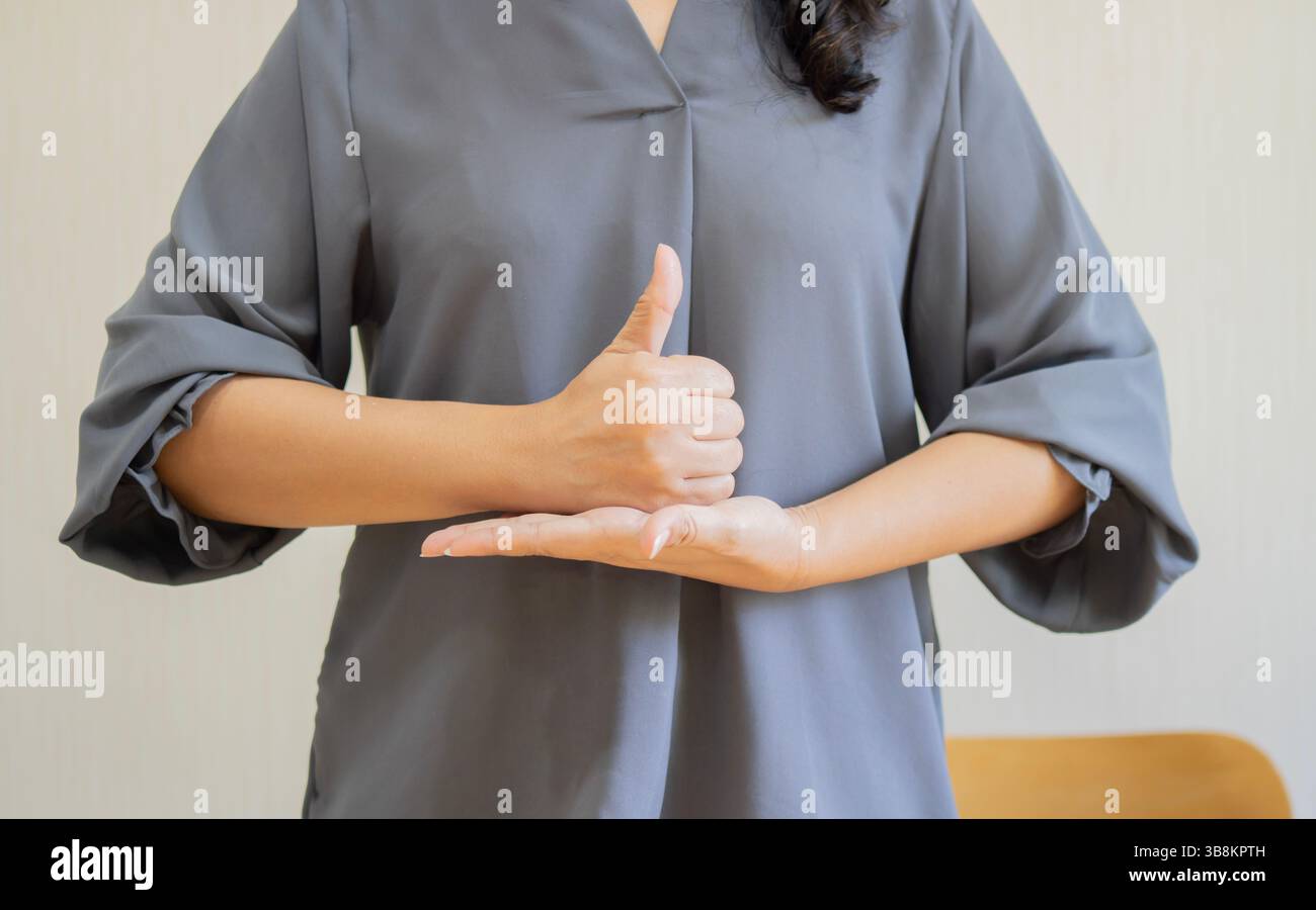 Beschnittene Aufnahme einer jungen taubstummen Frau mit Gebärdensprache auf beigefarbenem Hintergrund. Nahaufnahme. Stockfoto