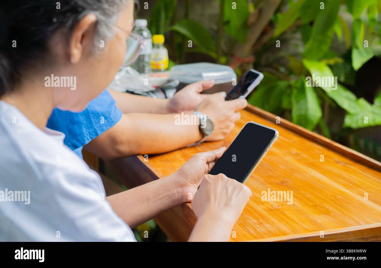 Zugeschnittenes Bild einer Hand, die ein Mobiltelefon hält, mit leerem schwarzen Bildschirm in einem Vintage-Café und unscharfem asiatischen Mann, der im Hintergrund sitzt Stockfoto