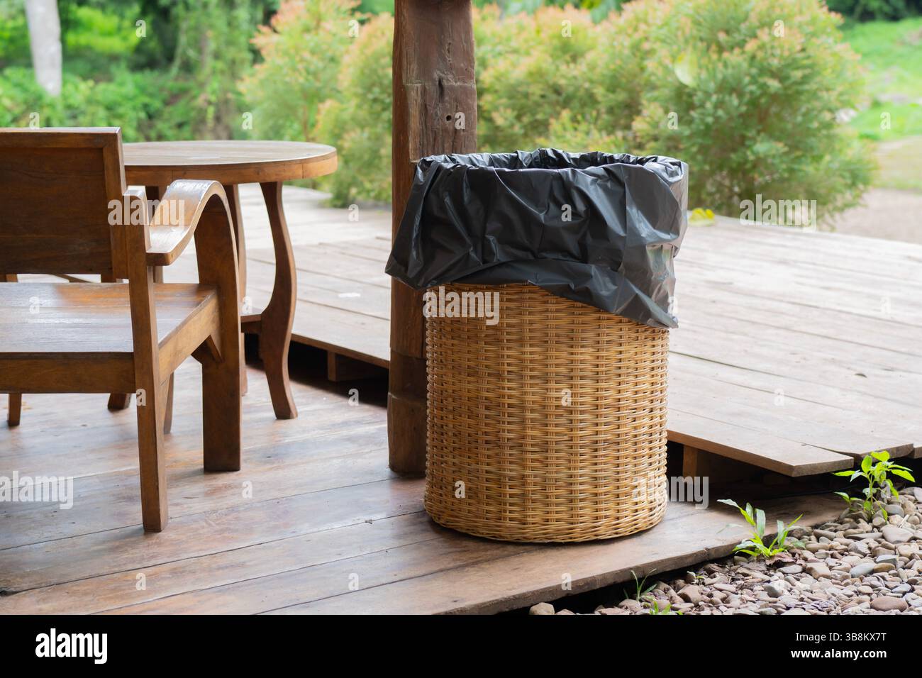 Schwarzer Plastikmüllbeutel in einem Bambuskorb in einem lokalen Naturcafé. Papierkorb Aus Bambus. Verschmutzungskonzept. Stockfoto