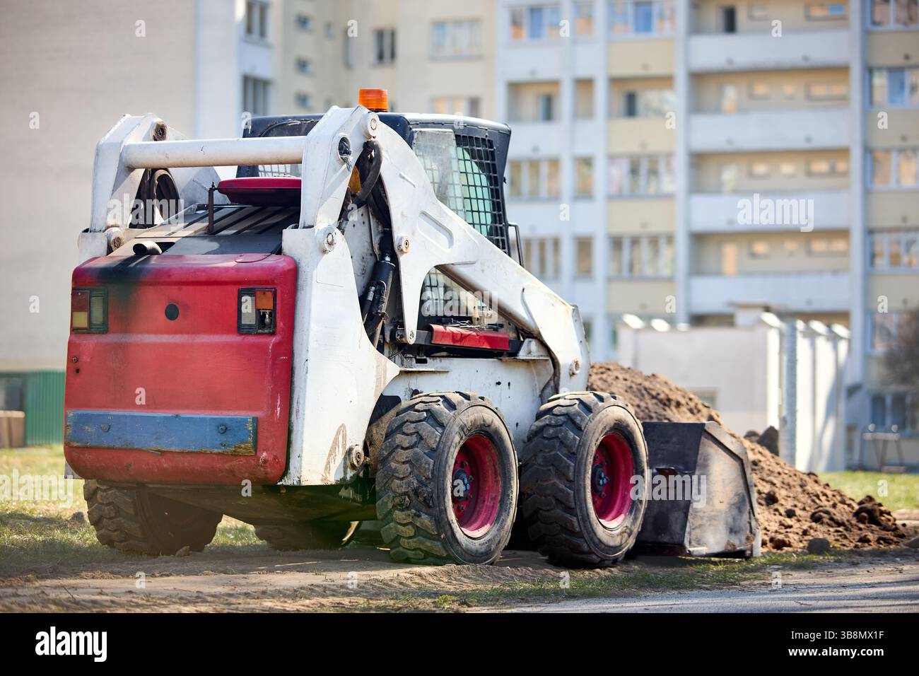 Ein alter schmutziger, rostiger Mini-Planierraupenbagger in der Nähe der Straße über urbanem Hintergrund mit einem selektiven Copyspace-Fokus von drei Vierteln Stockfoto