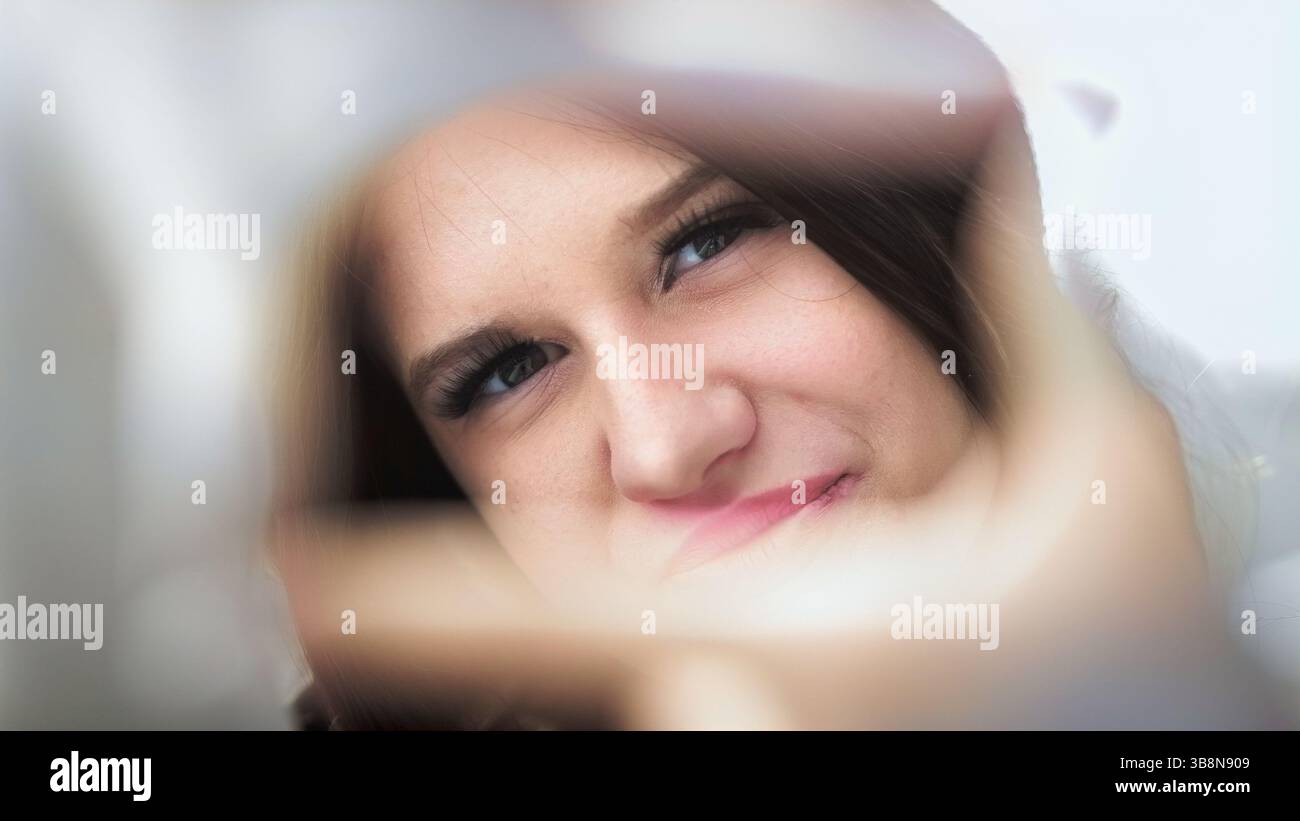 In einem stilvollen Moment zieht ein junges Mädchen die Aufmerksamkeit auf sich, indem es durch einen kreativen Rahmen posiert und ihr modisches Outfit und ihren selbstbewussten Ausdruck betont. Stockfoto