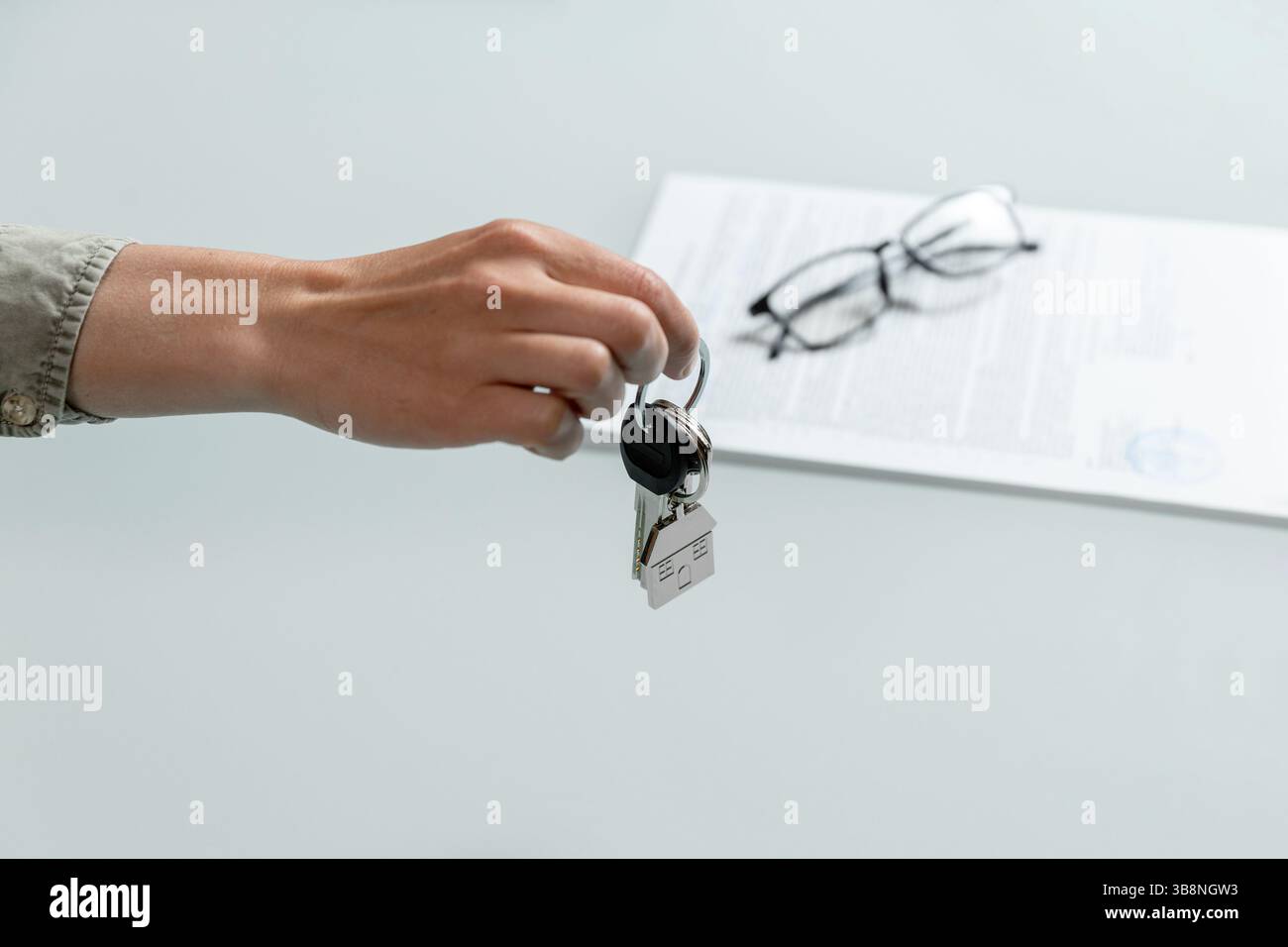 Weibliche Hand hält die Wohnungsschlüssel, unterschriebene Miet- oder Kaufvereinbarung auf einem Hintergrund. Immobilienbearbeitungskonzept Stockfoto