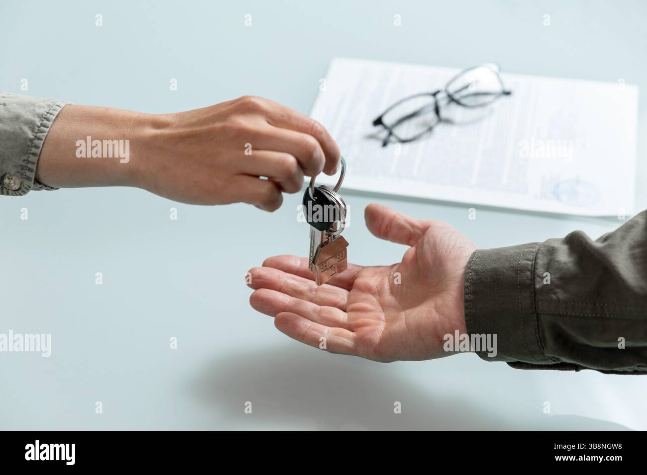 Weibliche Hand hält die Wohnungsschlüssel, unterschriebene Miet- oder Kaufvereinbarung auf einem Hintergrund. Immobilienbearbeitungskonzept Stockfoto