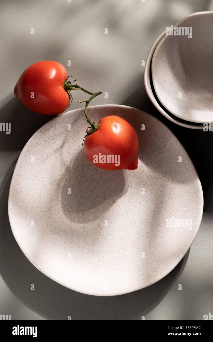 Flache Lagen aus grauen monochromen Tellern und Tomaten. Kulinarisches Konzept mit Platz für Text Stockfoto
