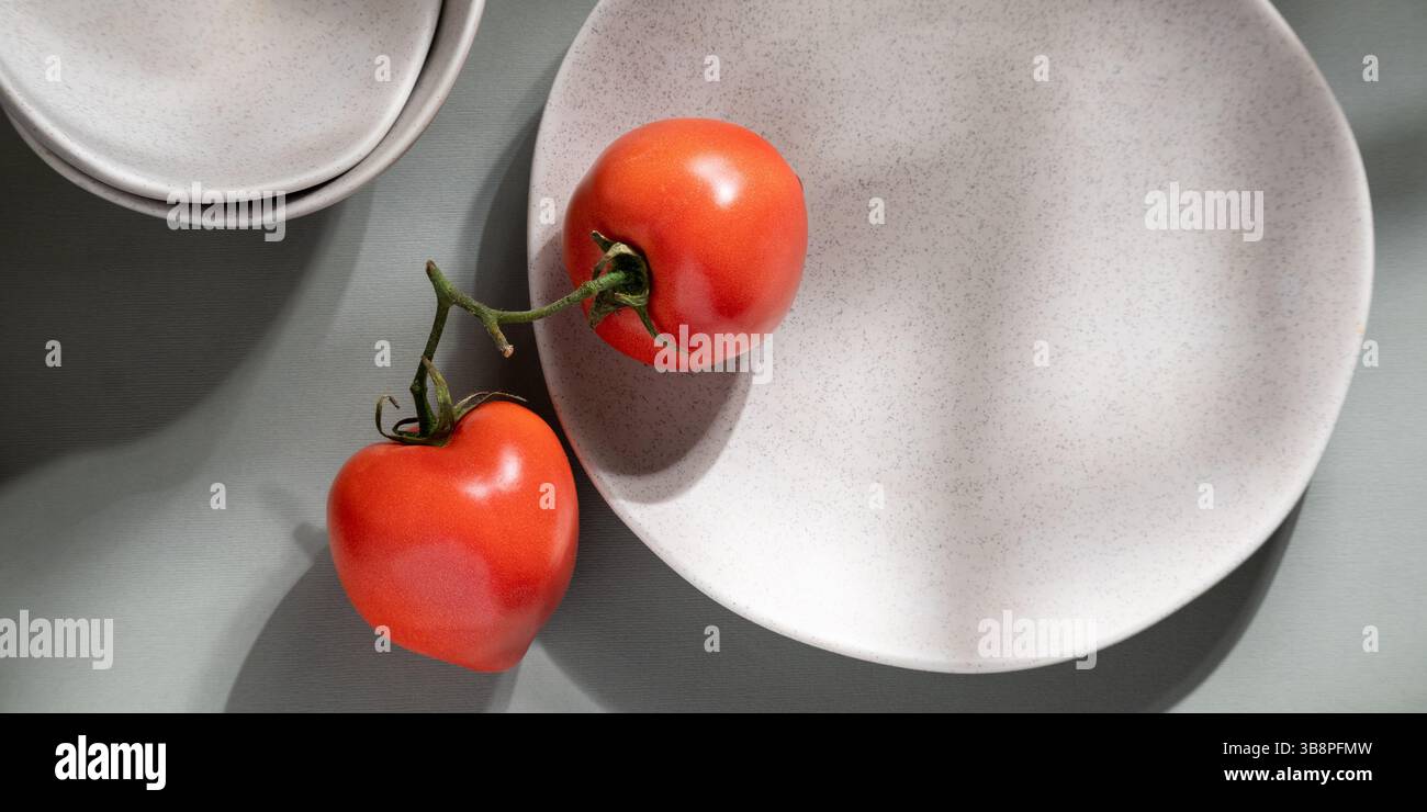 Flache Lagen aus grauen monochromen Tellern und Tomaten. Kulinarisches Konzept mit Platz für Text Stockfoto