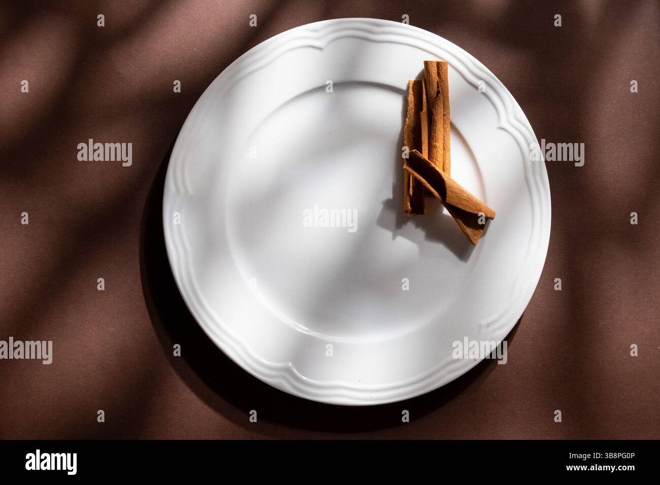 Weiße Keramik-Dessertteller mit Zimt auf braunem Hintergrund. Lebensmittelkonzept mit Platz für Text Stockfoto
