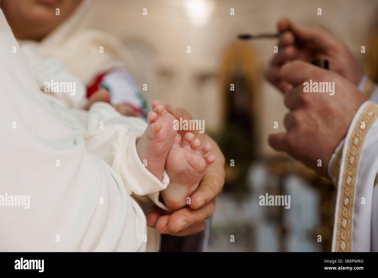 Ein zärtlicher Moment während der Taufzeremonie eines Babys, bei dem ein Priester den kleinen Fuß des Kindes mit heiligem Öl salbt, was für Reinigung und Akzeptanz steht Stockfoto