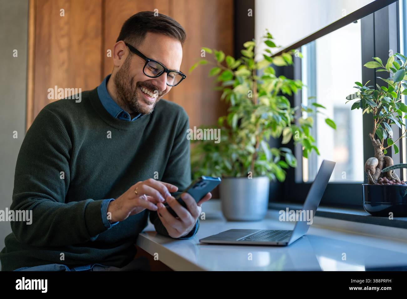 Selbstbewusster, lächelnder Geschäftsmann mit Smartphone im Heimbüro. Neue E-Mails werden geprüft. Videoanruf, Online-Kommunikationskonzept Stockfoto