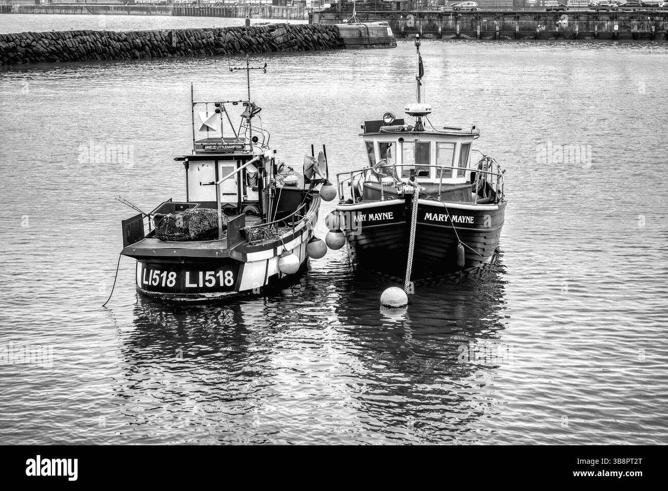 Zwei nebeneinander angedockte Fischereifahrzeuge legen bei Flut im Folkestone Harbour an und sind in einem auffälligen Schwarz-weiß-Ton dargestellt Stockfoto