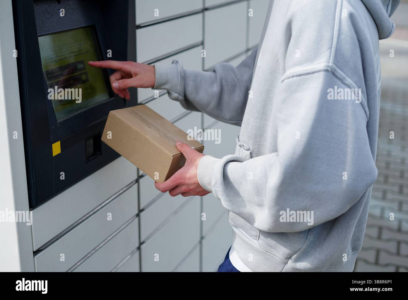 Ein junger Mann holt mit Touchscreen ein Papppaket aus einem Selbstbedienungs-Paketschließfach ab Stockfoto