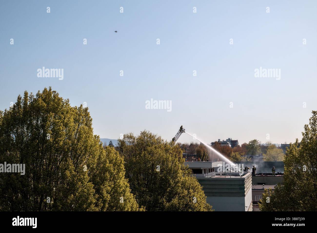 Feuerwehrmann löscht einen Gebäudebrand auf Leiter und Dach. Tagsüber brennende Geschäftshäuser in der Stadt. Luftdrohne schwebt über Asse Stockfoto