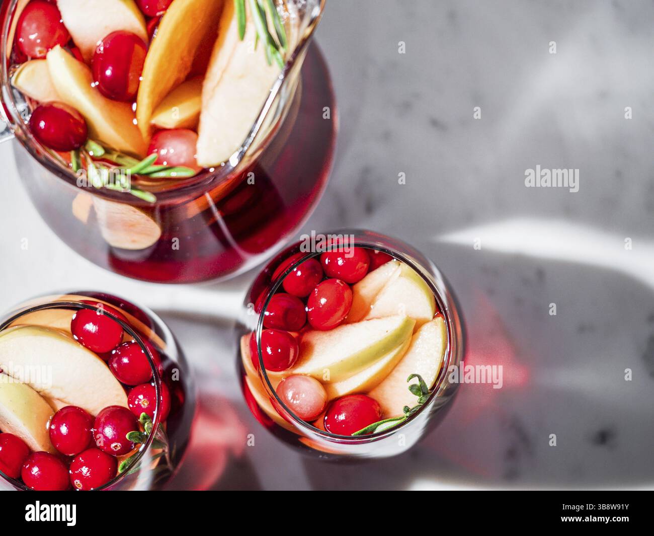 Wintersangria auf Tischplatte mit grauer Leinentischdecke. Gläser Sangria mit Fruchtscheibe, Cranberry und Rosmarin. Platz für Text oder Design kopieren. Oben Stockfoto