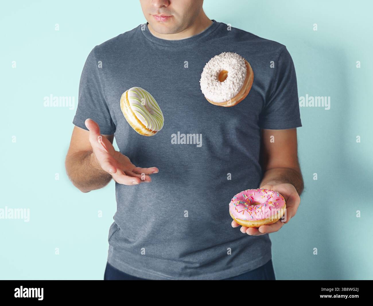 Jongleur Mann jongliert Donuts auf blauem Hintergrund. Donuts Lieferung oder ungesunde Diät-Konzept. Fliegende glasierte Donuts mit Streuseln und Trockenkokonu Stockfoto