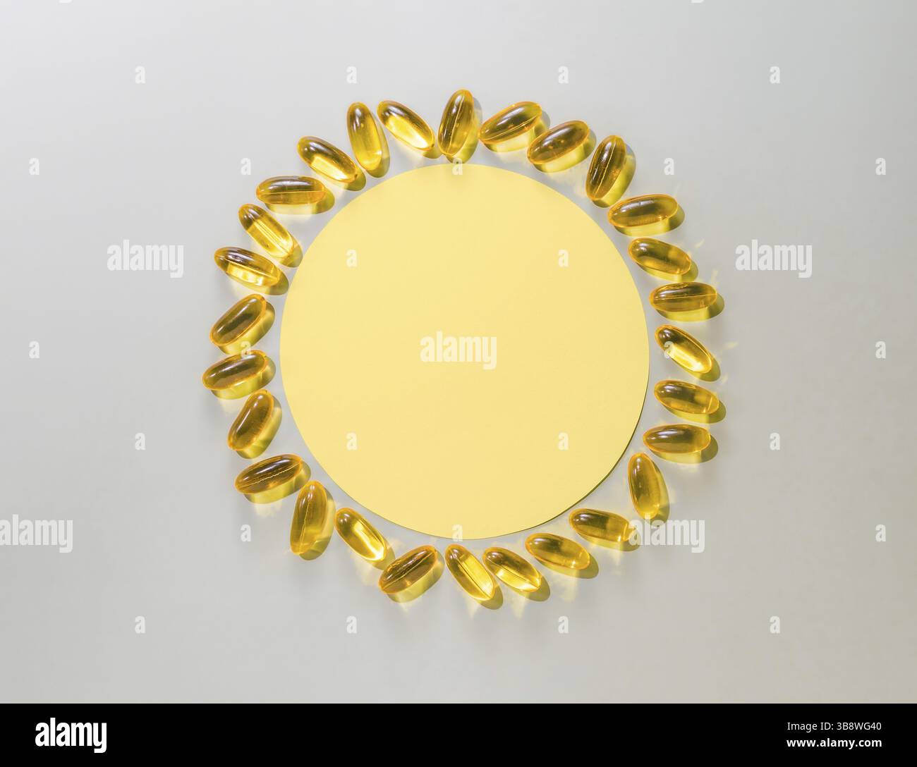 Vitamin-D3-Flüssigkapseln um einen gelben Kreis auf neutralgrauem Hintergrund. Draufsicht oder flache gelbe Sonne mit Papierkreis und Flüssigkapseln Stockfoto