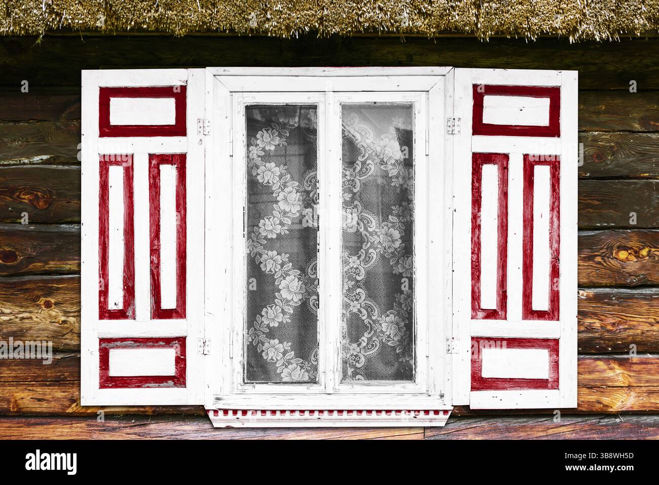 Traditioneller rustikaler Fensterrahmen. Weißer Holzrahmen mit roten Fensterläden. Spitzenvorhang hinter Glas. Alte Landkabinenwand. Volksarchitektur. Stockfoto