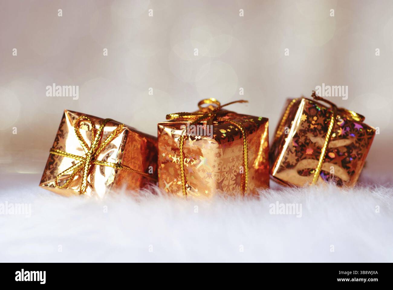 Goldene Weihnachtsgeschenke auf weißem Pelz und Hintergrund mit unscharfen goldenen Lichtern. Oberer Freiheitsgrad Stockfoto