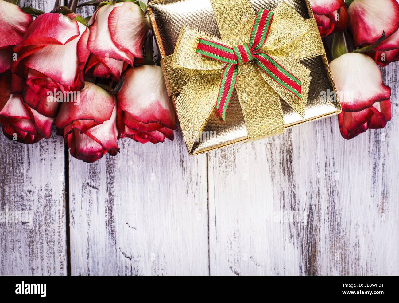 Goldene Geschenkbox und Rosenstrauß auf weißem, schubförmigem Holzhintergrund Stockfoto