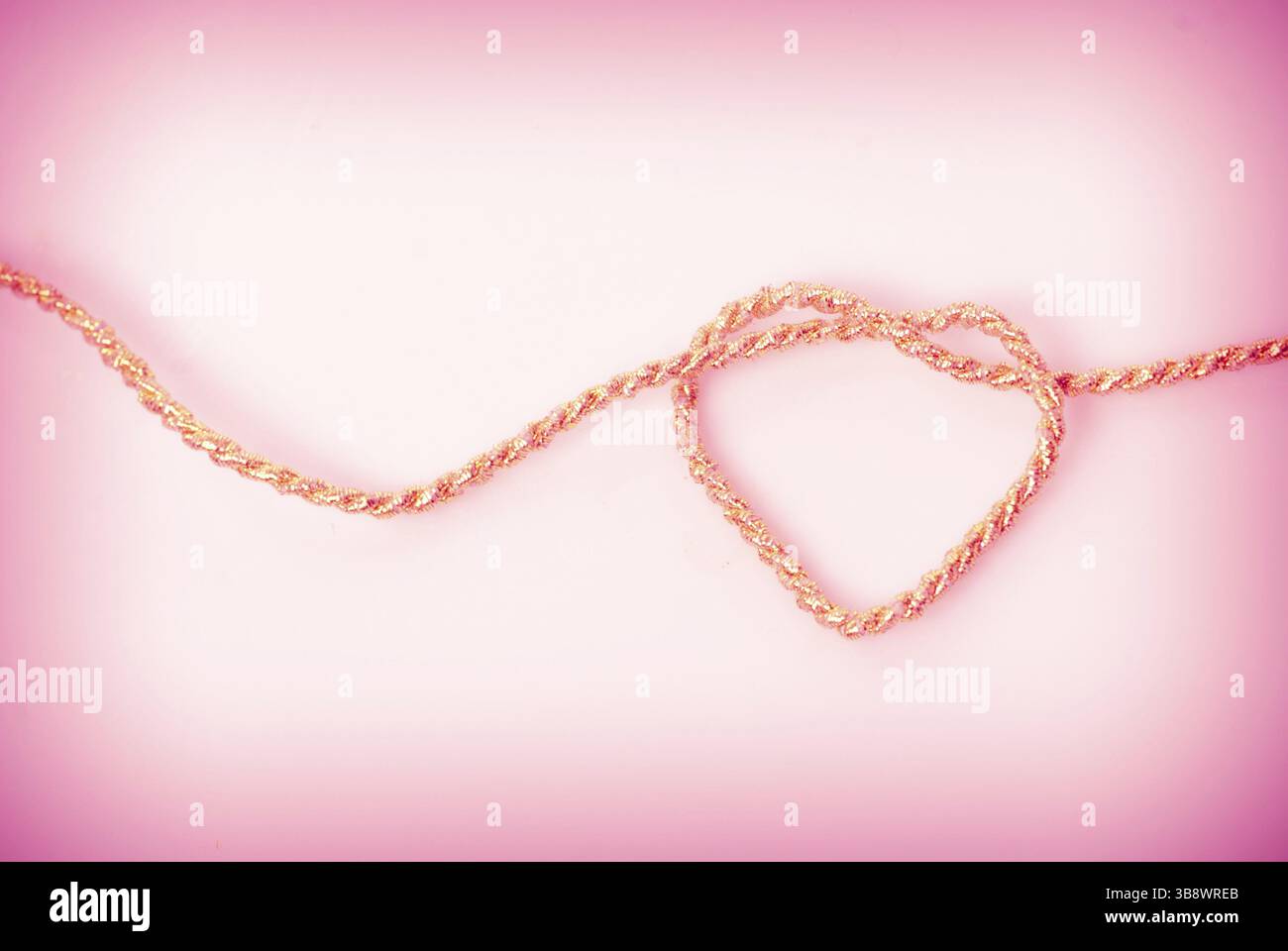Herzform aus gold Seil auf rosa Hintergrund. Liebe Postkarte Stockfoto