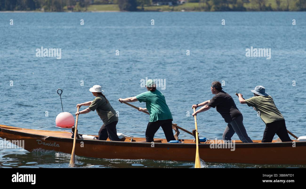 Vier-Personen-Team paddelt synchron auf einem ruhigen See, umgeben von Grün unter blauem Himmel in einem hölzernen Kanu Stockfoto