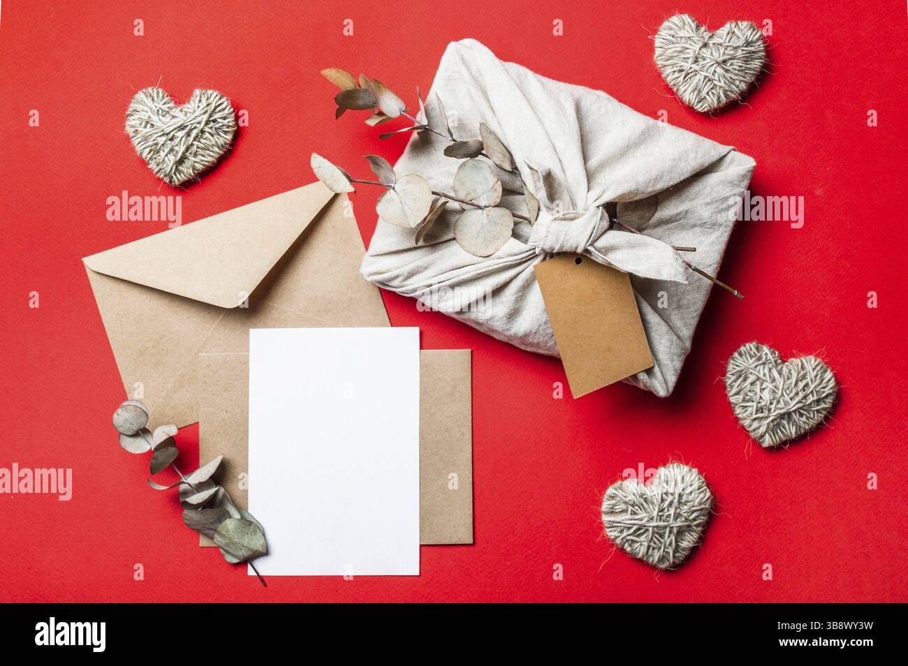 Zero Waste Valentinstag-Konzept und Moon-up auf Rot. Umweltfreundliche Geschenktücher im Furoshiki-Stil, Papierumschlag aus Bastelpapier, leere Grußkarte Stockfoto