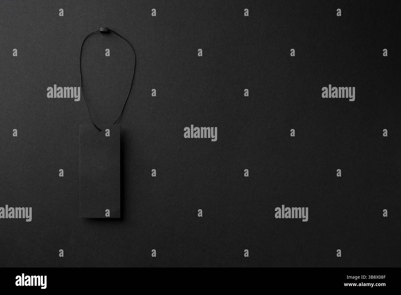 Leerer schwarzer Pappanhänger mit Schnur auf schwarzem Hintergrund Stockfoto