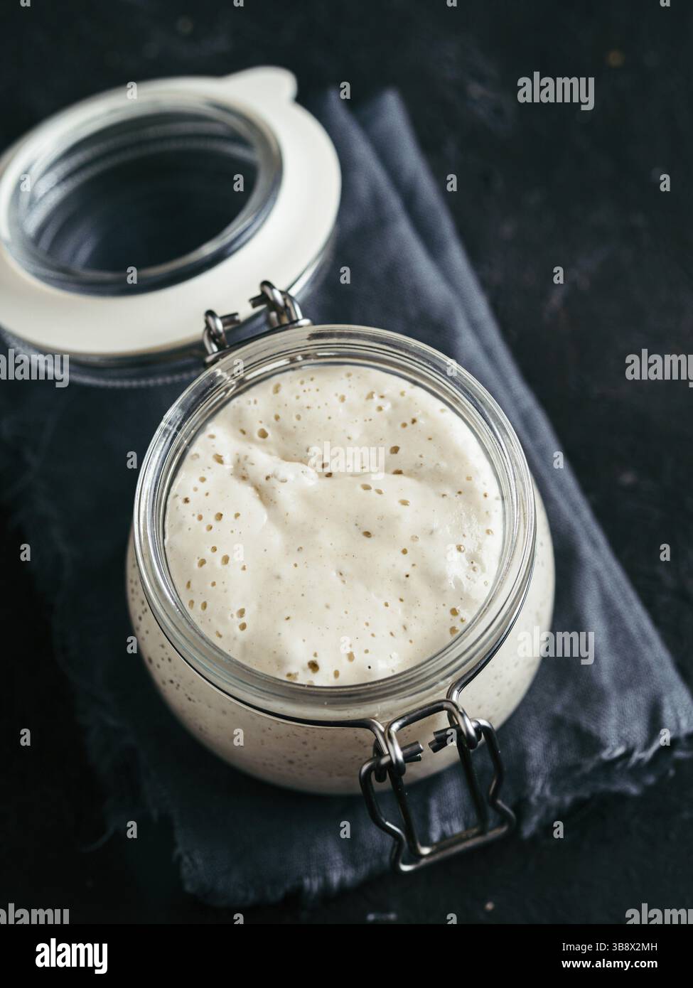 Vorspeise aus Weizensauerteig. Glasbehälter mit Sauerteigstarter auf dunklem Hintergrund, Kopierraum. Vertikal Stockfoto