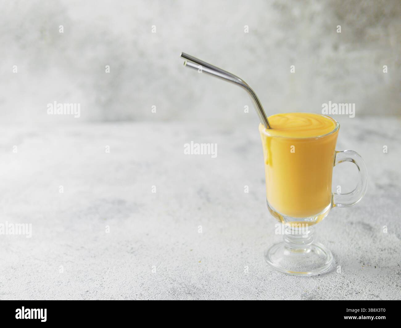 Gelbe mango Joghurt oder Smoothie auf grauem Zement Hintergrund mit Kopie Raum gelassen. Gelbwurz Lassie oder Lassi in Glas mit Metall Strohhalme Stockfoto