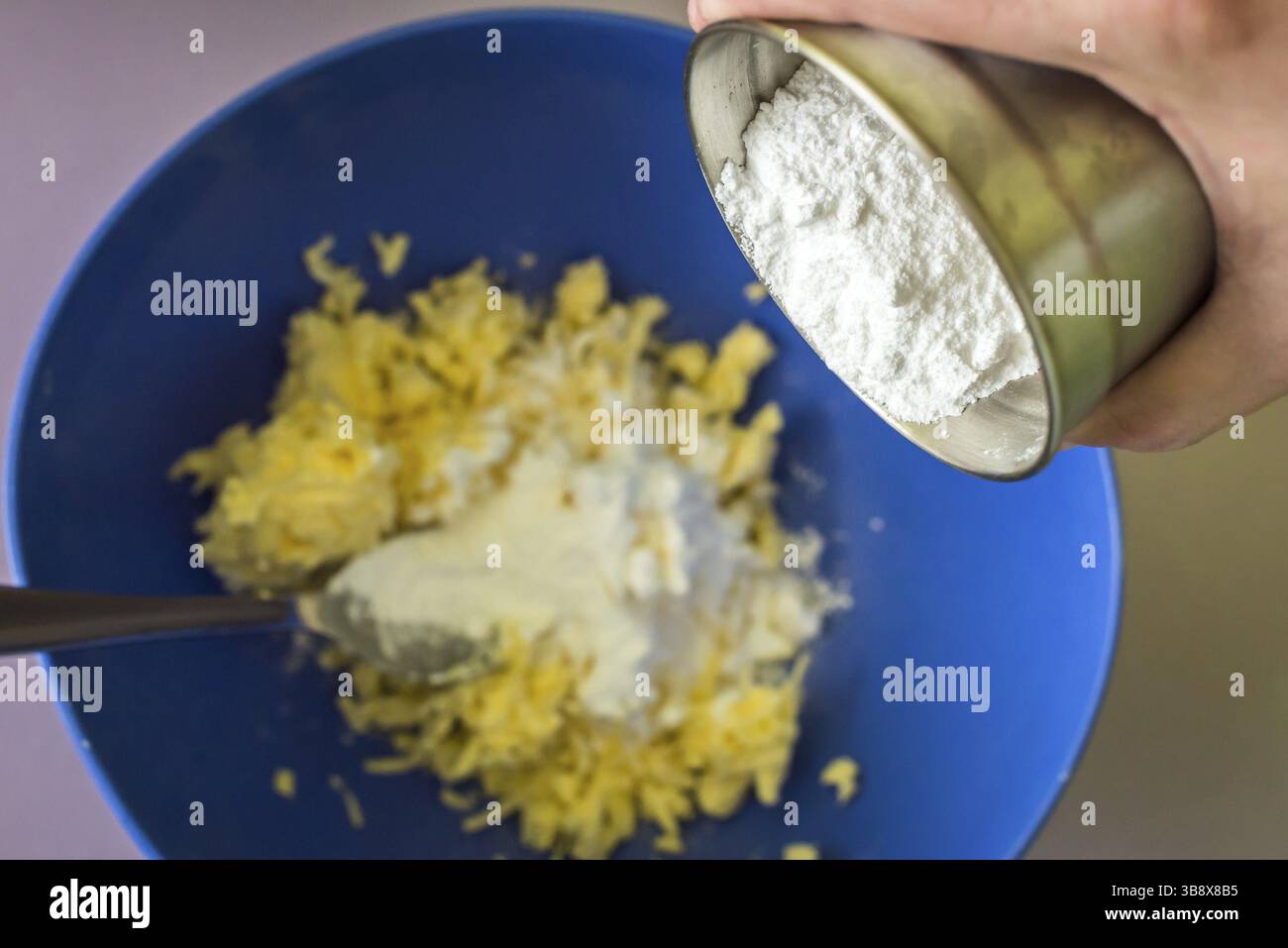 Geben Sie Puderzucker von Hand in Butter über die blaue Schüssel Stockfoto
