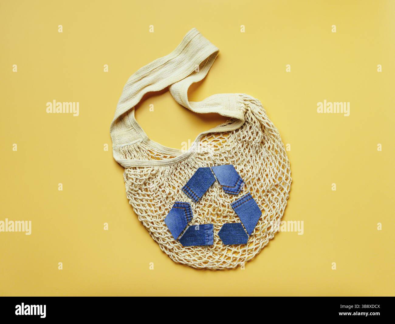 Wiederverwendung, Reduzierung, Recycling Konzept Hintergrund. Recycling-Symbol aus alten Jeans und Mesh-Tasche auf gelbem Hintergrund. Draufsicht oder flaches Lay. Speicherplatz kopieren für Stockfoto