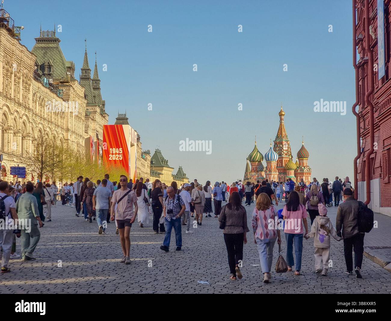 Menschen auf dem Roten Platz Moskau Russland, mit Dekorationen des Siegtages der Sowjetunion (2. Weltkrieg). Am 9. Mai 2025; Basilius-Kathedrale im Rücken - Smartphone-aufgenommenes Stockfoto