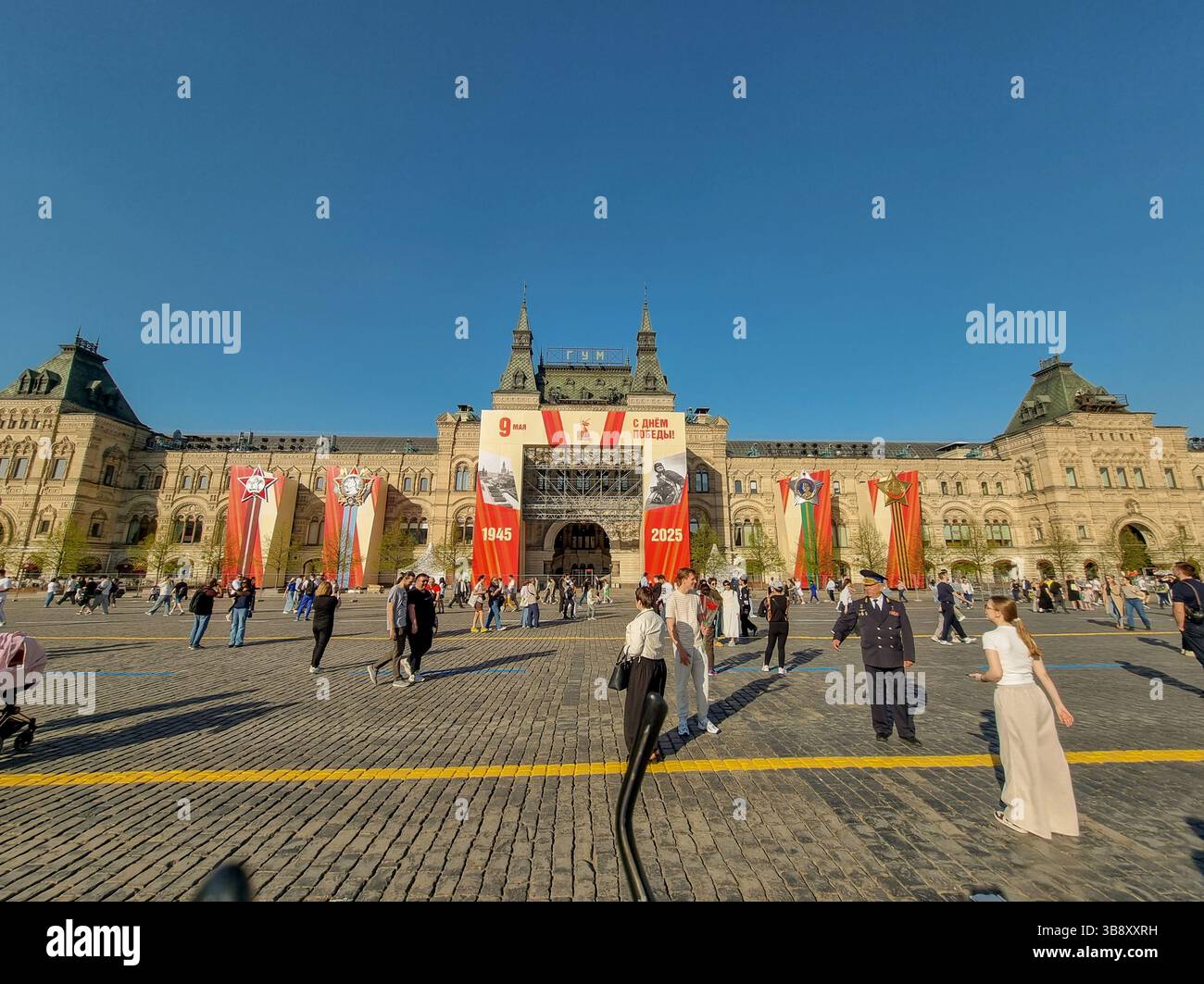Menschen auf dem Roten Platz Moskau Russland, mit Dekorationen des Siegtages der Sowjetunion (2. Weltkrieg). Am 9. Mai 2025; dekoriertes KAUGUMMI im Hintergrund - Smartphone-aufgenommenes Stockfoto