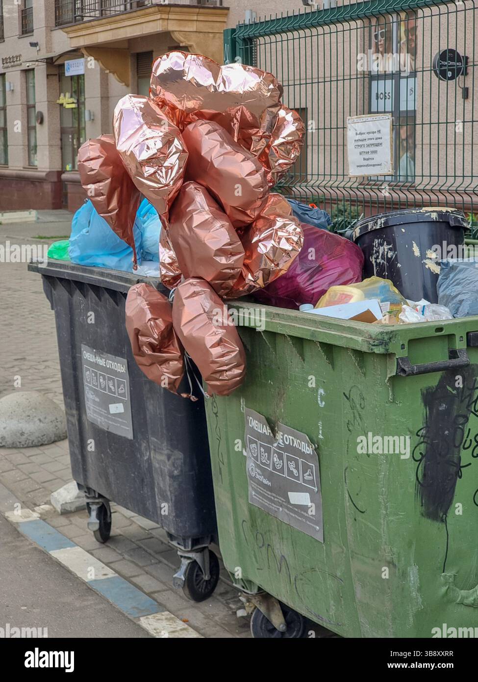 Glänzende, metallische, herzförmige Partyballons, die im Abfallbehälter stehen; Konzept des Zerbrechens, der verlorenen Liebe, des Endes der Beziehung, des Endes der Party Stockfoto