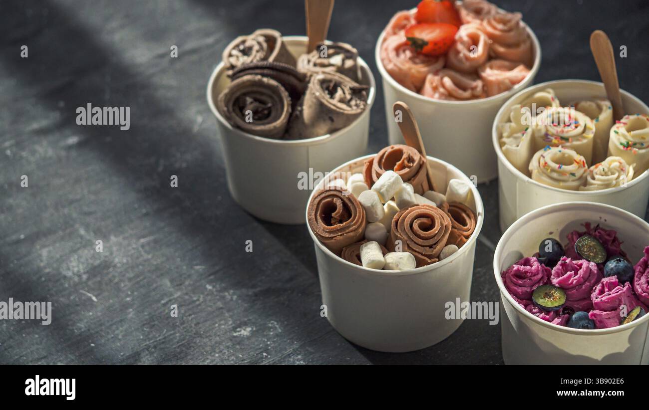 Gerolltes Eis in Kegelbecher auf dunklem Hintergrund. Verschiedene Eisrollen oder Thai Stil gerolltes Eis mit Kopierraum für Text oder Design. Banner. Natu Stockfoto