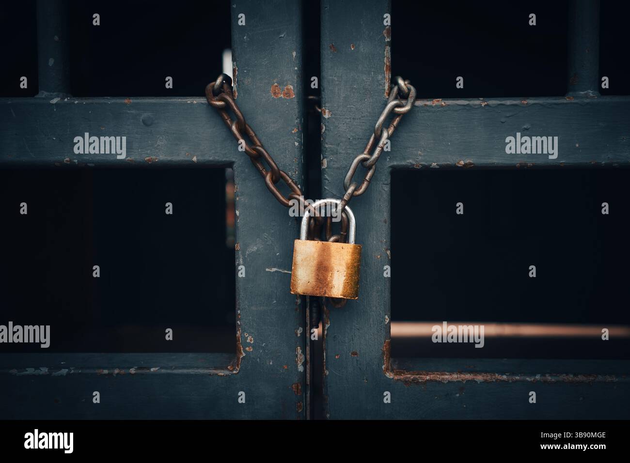 Ein bronzenes Metallschloss an einer Kette zwischen den rostigen Stäben eines alten Zauns. Stockfoto