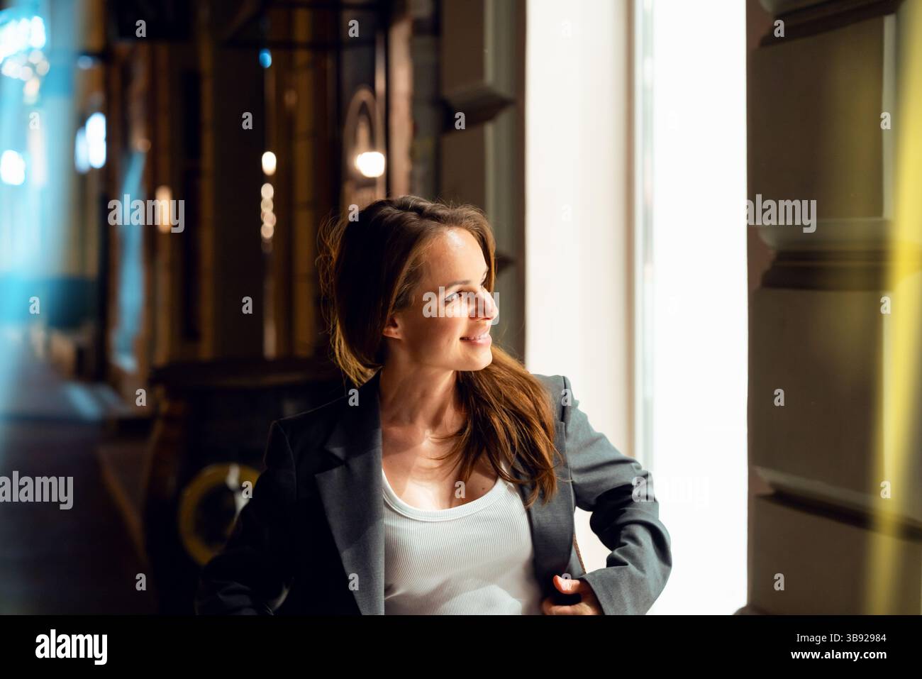 Modische, städtische Frau, die nachts spaziert und auf ein beleuchtetes Schaufenster blickt Stockfoto