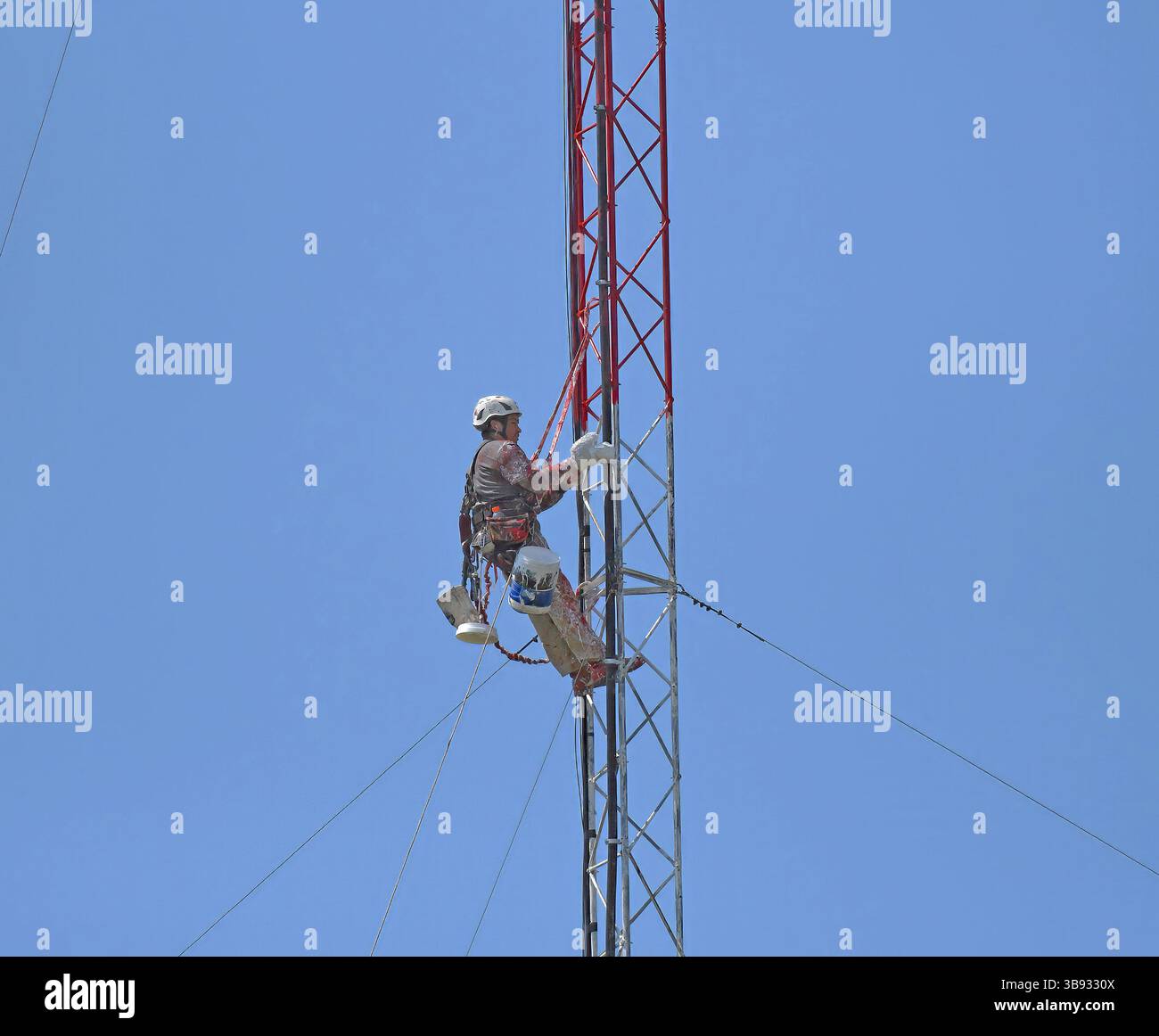 EMPORIA KANSAS, USA - 8. MAI 2025 der Turmtechniker, der mit Sicherheitsseilen in etwa 200 m Höhe an einem Funkturm eingehängt ist, verwendet einen Malhandschuh, um die Querträger weiß zu malen Stockfoto