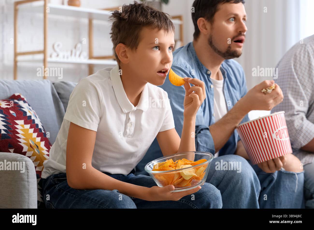Fröhliche Familienessen, während man zuhause Fußballspiele auf dem Sofa ansieht Stockfoto