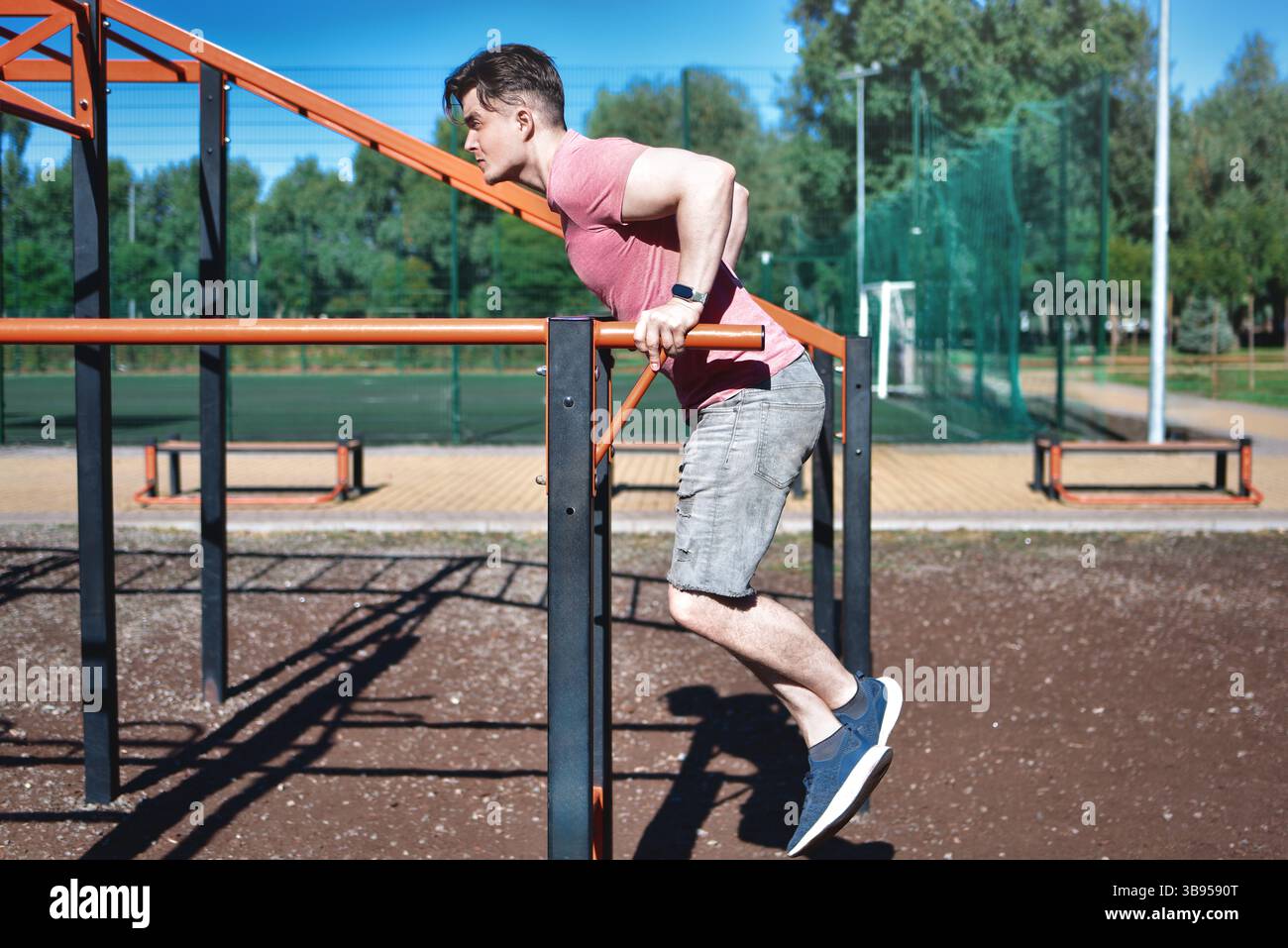 Ein junger Mann wird an einem sonnigen Tag in einem Outdoor-Workout-Bereich Dips an parallelen Bars gezeigt. Er konzentriert sich auf seine Übung und demonstriert Stärke Stockfoto