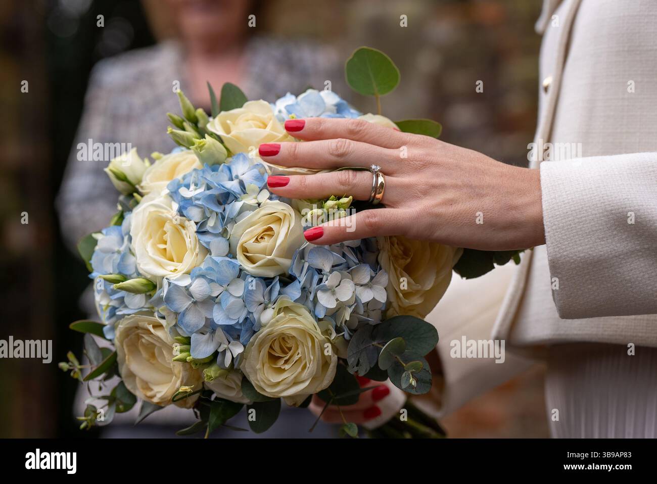Damenhand mit roten Nägeln, die einen Haufen blauer und weißer Blumen halten Stockfoto