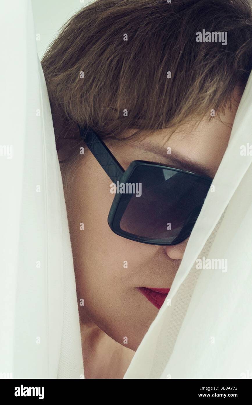 Ein Porträt einer erwachsenen brünetten Frau mit kurzen Haaren, die eine schwarze Brille mit einem halb verborgenen Gesicht trägt Stockfoto