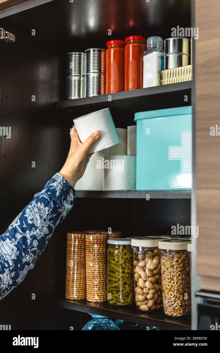 Nahaufnahme von nicht erkennbarer weiblicher Hand, die Toilettenpapier zur Notversorgung in der Küche füllt, Vorbereitung auf mögliche Katastrophen. Warnung, Weitblick A Stockfoto