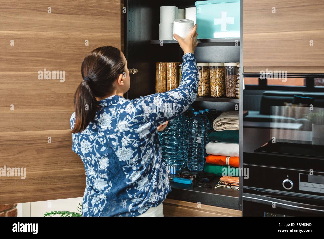 Nicht erkennbare Frau, die 72 Stunden Überlebenskit für mögliche Katastrophen vorbereitet. Frau, die Toilettenpapier in die Vorratskammer in der Küche legt. Stockfoto
