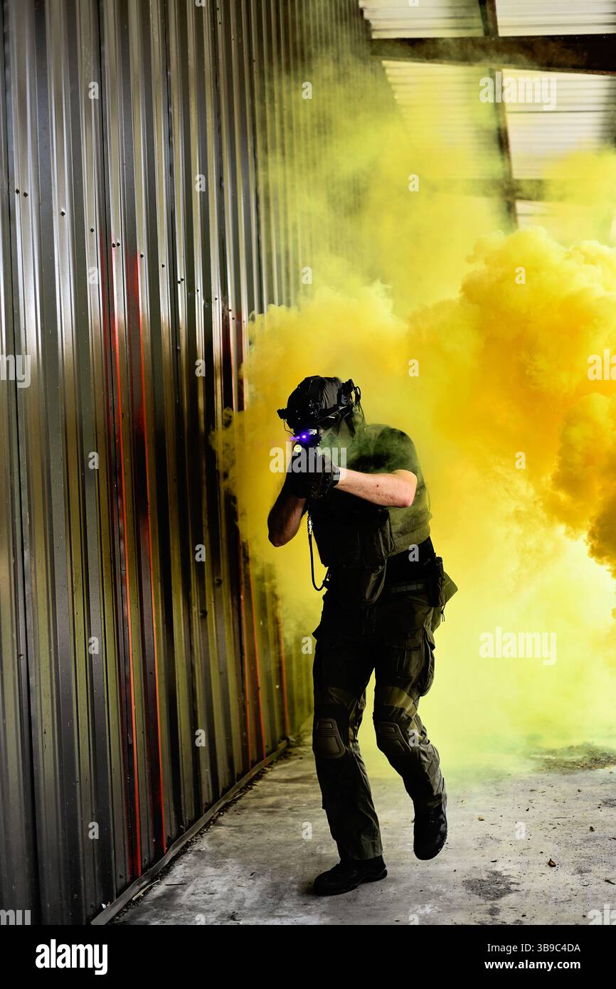 Bewaffneter männlicher Airsoft-Spieler, der durch gelben Rauch läuft Stockfoto