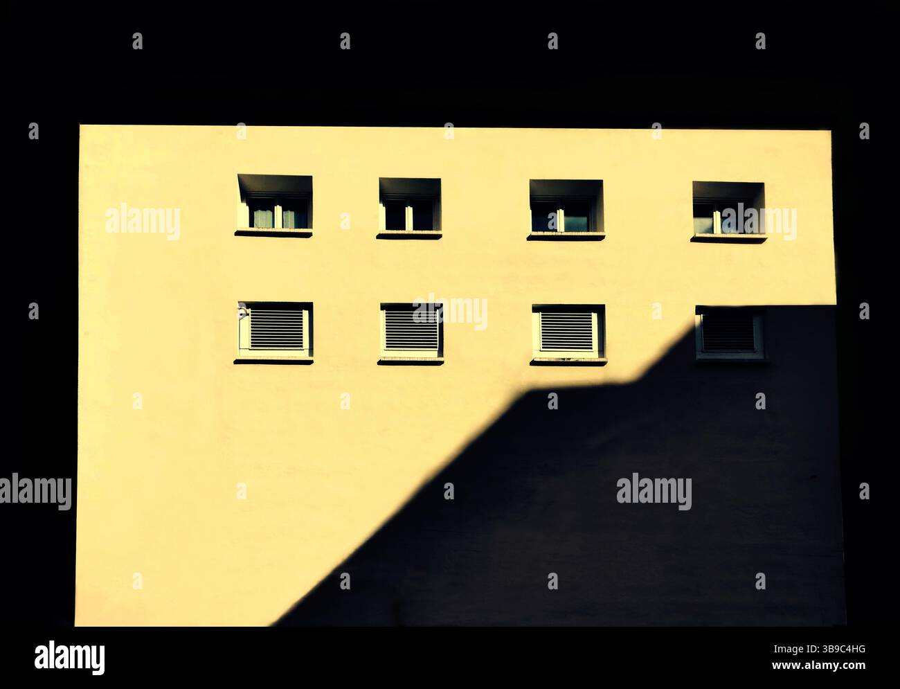 Die hellgelbe Wand eines Gebäudes wird von einem tiefen Schatten kontrastiert, was ein eindrucksvolles Bild erzeugt. Fenster zeigen eine Reihe von Details an Stockfoto