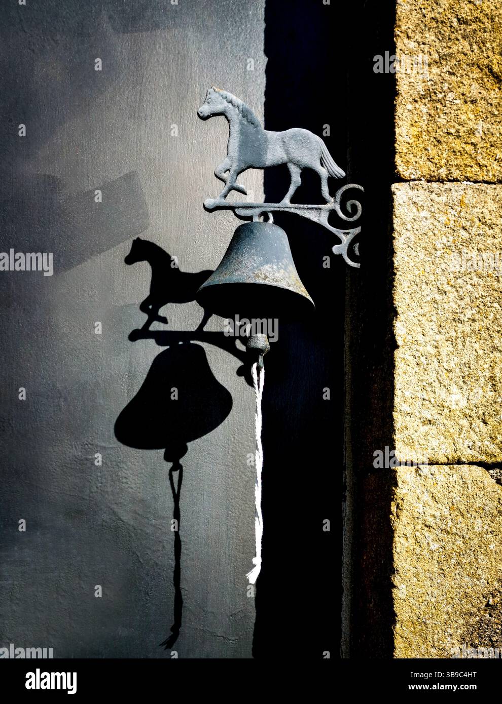 Eine dekorative Glocke in Form eines Pferdes hängt an einer dunklen Wand und erzeugt einen einzigartigen Schatten. Das charmante Merkmal verleiht der rustikalen Umgebung während des Aufenthalts Charakter Stockfoto