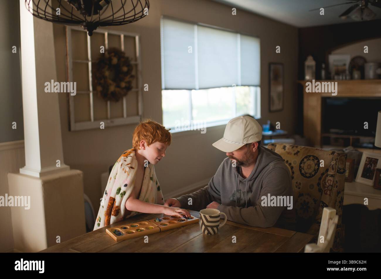 Vater und Sohn verbinden sich über Brettspiel in gemütlicher, sonnendurchfluteter Atmosphäre Stockfoto