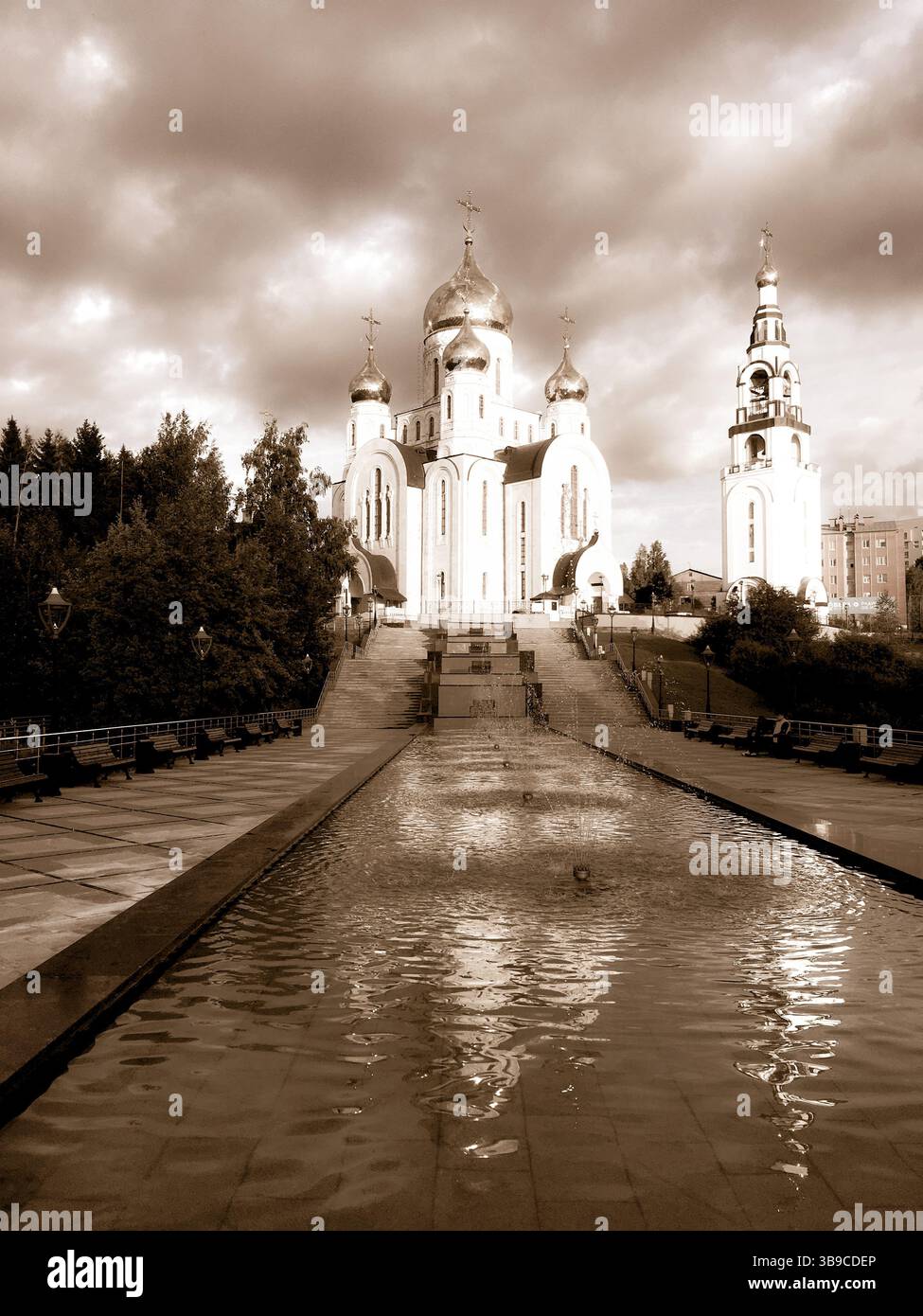 Eine große orthodoxe Kathedrale mit kunstvollen Kuppeln steht majestätisch unter einem dramatischen Himmel, der sich in einem langen Pool spiegelt, der sich darauf erstreckt. Stockfoto