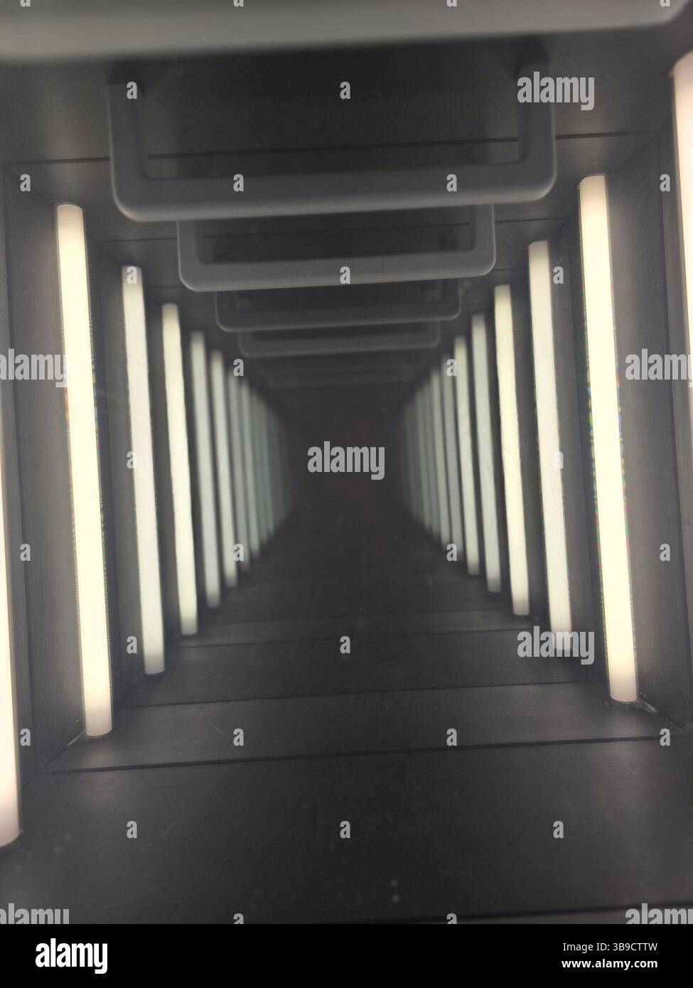 Das Bild zeigt eine optische Illusion eines scheinbar unendlichen Tunnels, der durch parallele Reihen weißer LED-Leuchten entsteht, die auf Spiegeln reflektieren. - Smartphone-aufgenommenes Stockfoto